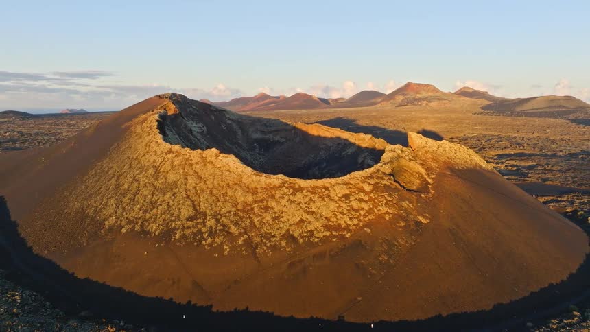 Stunning aerial pull-back shot reveals the El Cuervo volcano crater in Lanzarote, bathed in the warm light of the golden hour