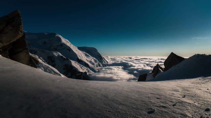 Majestic timelapse of shadows and light moving across a snowy mountain range above a sea of clouds