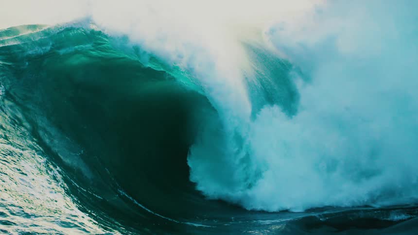 A massive and powerful teal ocean wave crests and crashes with immense force in ultra slow motion