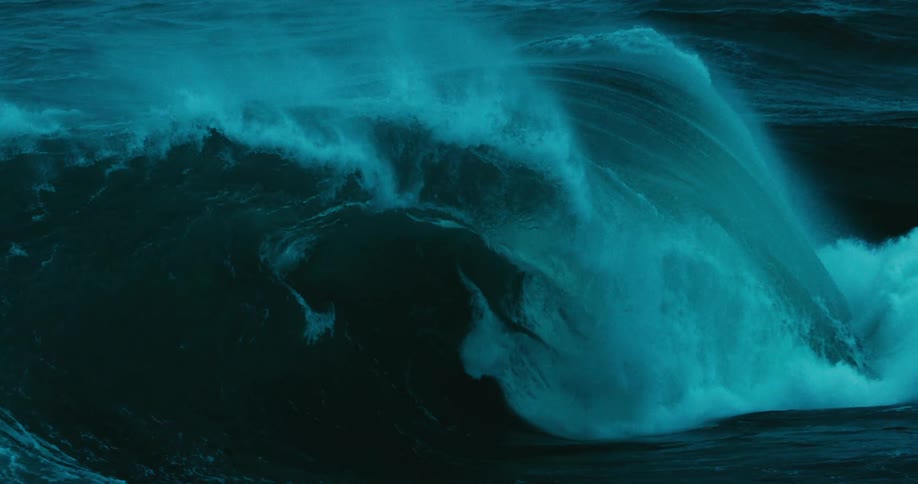 A majestic slow-motion shot captures a massive teal-colored ocean wave cresting and breaking with immense power