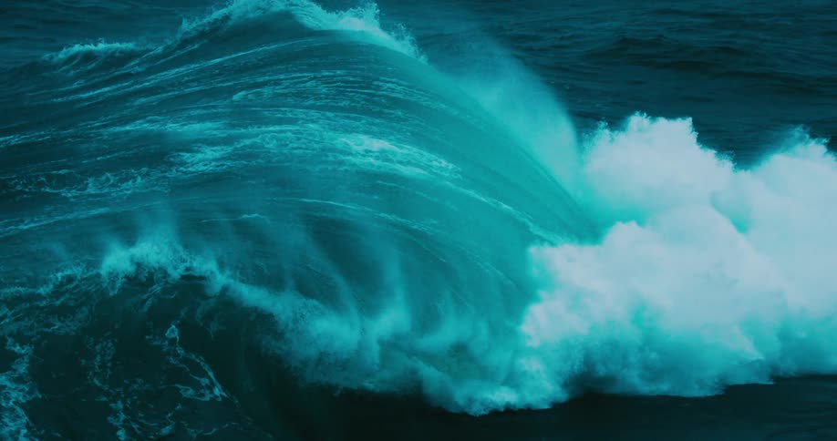 A powerful and dramatic slow-motion close-up of a massive turquoise ocean wave curling and breaking