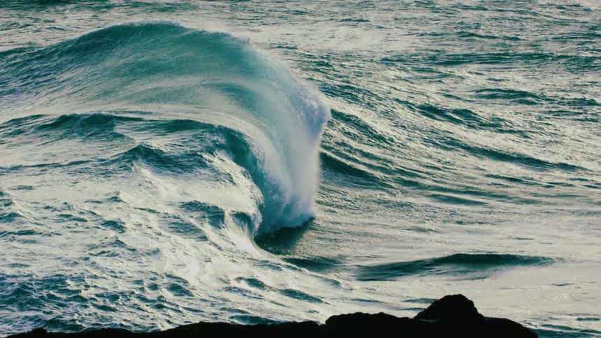 A powerful turquoise ocean wave forms and crashes in dramatic slow motion