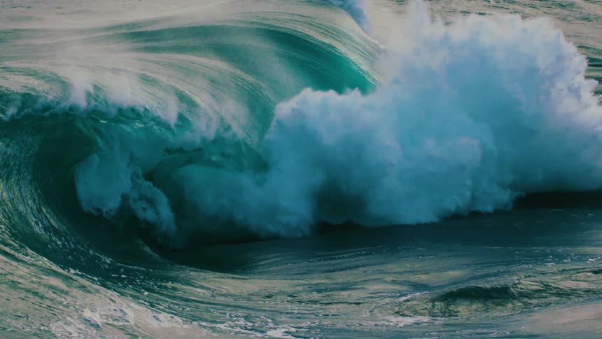 A powerful turquoise ocean wave curls into a perfect barrel before crashing in dramatic slow motion
