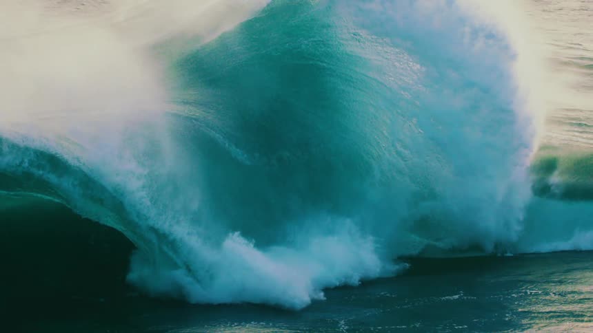 The immense power of the ocean is captured as a giant teal wave crashes in dramatic slow motion