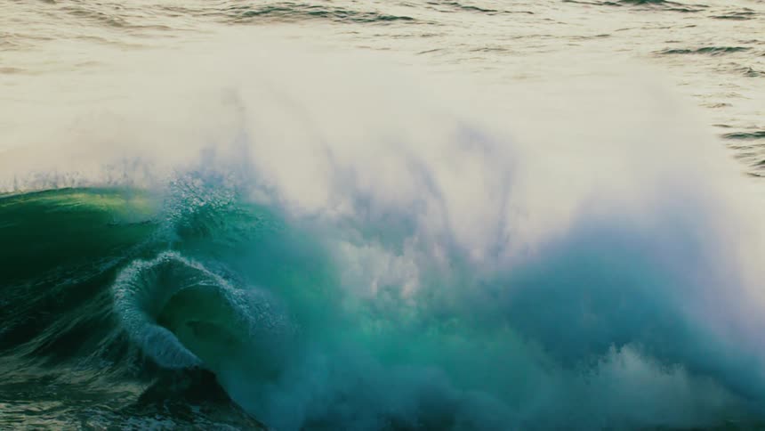 A breathtaking slow-motion view shows a massive, powerful emerald green ocean wave curling and crashing with immense force