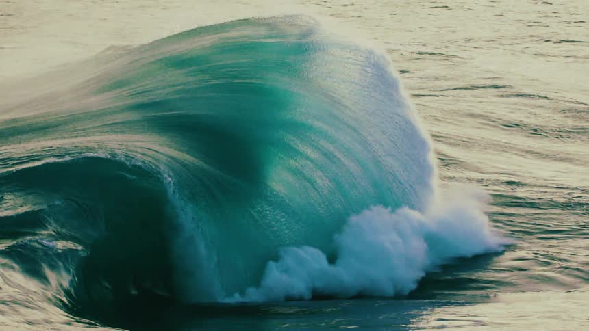 A powerful ocean wave curls and breaks in mesmerizing super slow motion, its teal water churning into white foam
