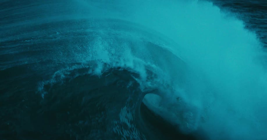 A powerful, moody teal-colored ocean wave curls and breaks in dramatic slow motion