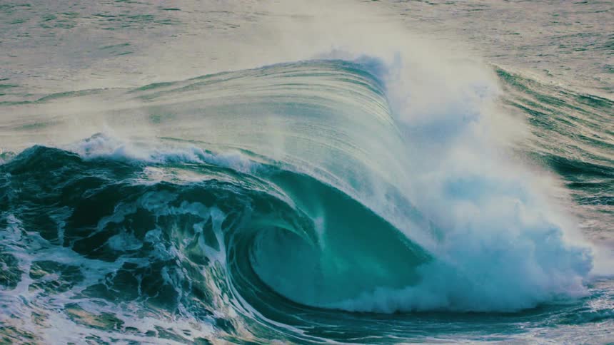 An epic slow-motion shot captures the raw power of a massive turquoise ocean wave as it curls and crashes