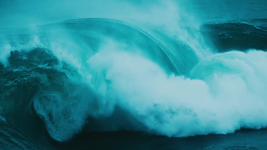 A massive, powerful teal-colored ocean wave crests and breaks in dramatic slow motion