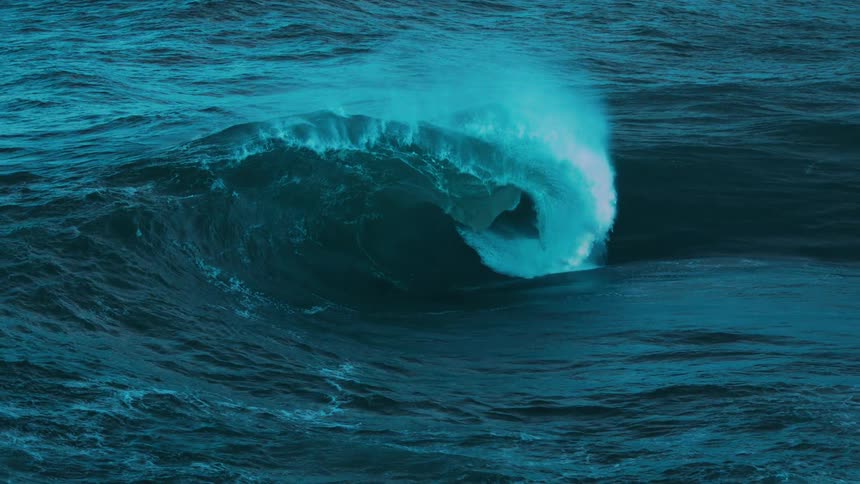 A massive turquoise ocean wave curls into a perfect barrel and crashes in mesmerizing slow motion