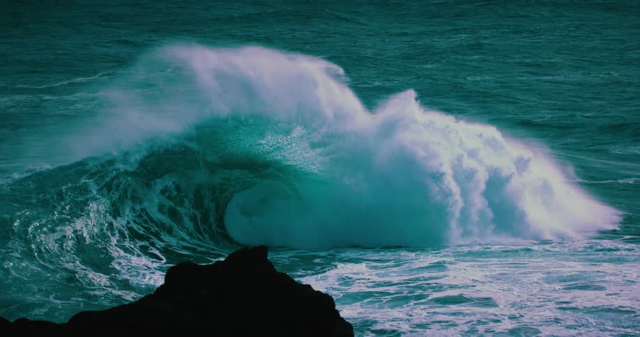 A massive, powerful ocean wave with turquoise hues curls and breaks in dramatic slow motion