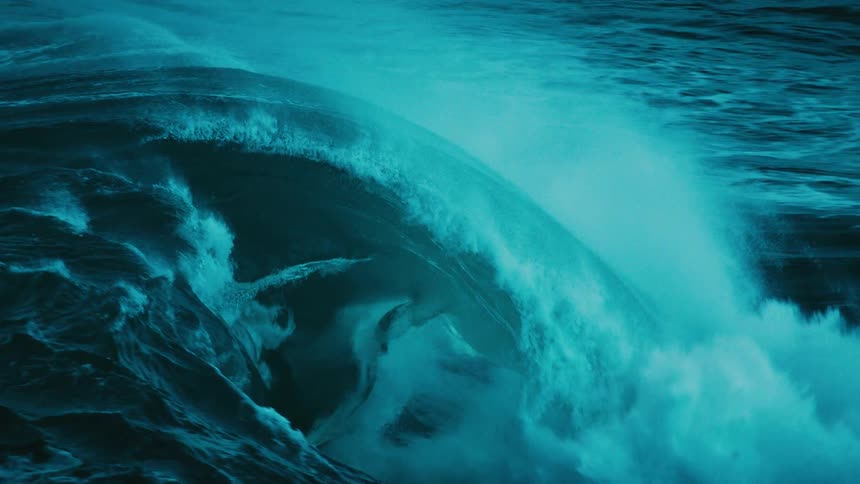A massive, teal-colored ocean wave crests and crashes in dramatic slow motion