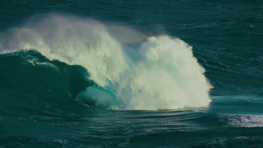 A massive teal ocean wave curls and crashes in dramatic slow motion, creating a spectacular display of whitewater and spray