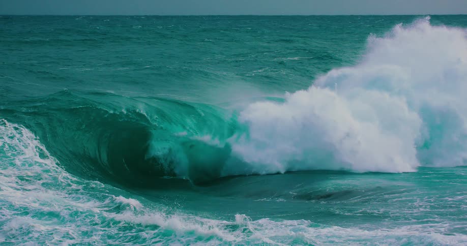A powerful turquoise ocean wave forms a barrel and crashes in dramatic slow motion, creating a spectacle of white spray