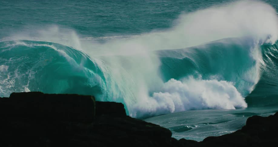 A massive turquoise ocean wave builds and crashes with immense power in dramatic slow motion