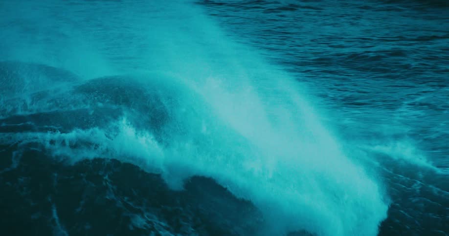 Slow motion footage shows a powerful, dark teal ocean wave as it forms, crests, and breaks