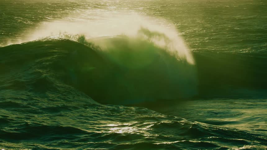 A majestically powerful green ocean wave curls and crashes in stunning slow motion, illuminated by golden light