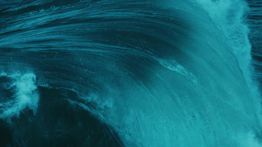 A powerful turquoise ocean wave swells and breaks in dramatic, super slow motion