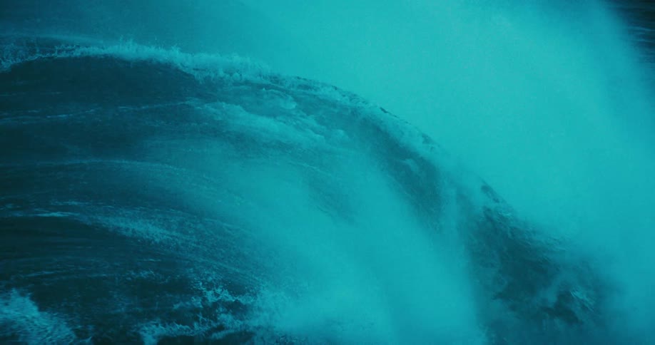 A powerful, dark teal ocean wave crashes in dramatic and mesmerizing slow motion