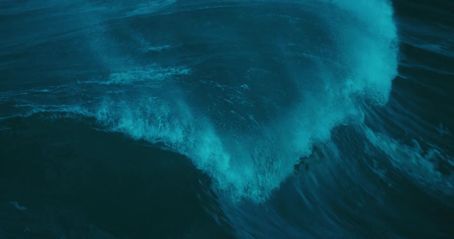 An immense and powerful turquoise ocean wave builds and crashes in dramatic slow motion