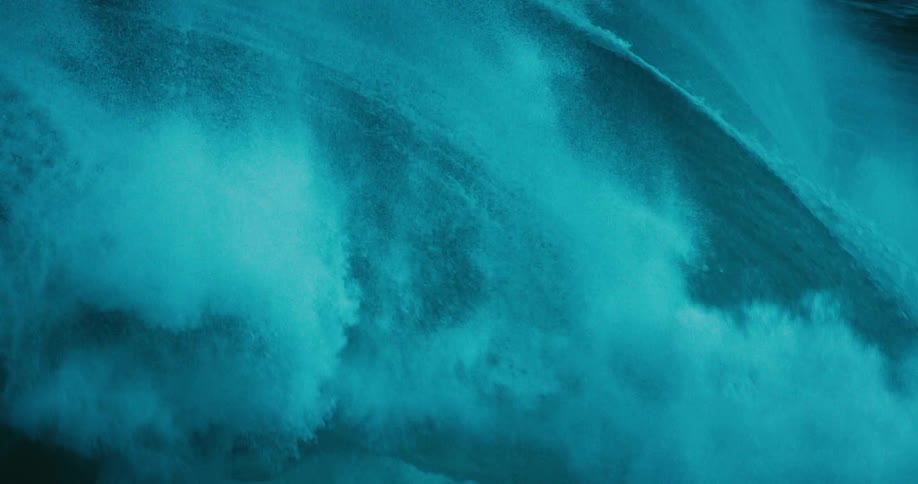 A dramatic slow-motion close-up captures a massive, dark teal ocean wave as it powerfully curls and crashes
