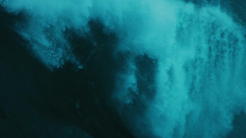 A powerful, giant teal-colored ocean wave swells and crashes in dramatic super slow motion