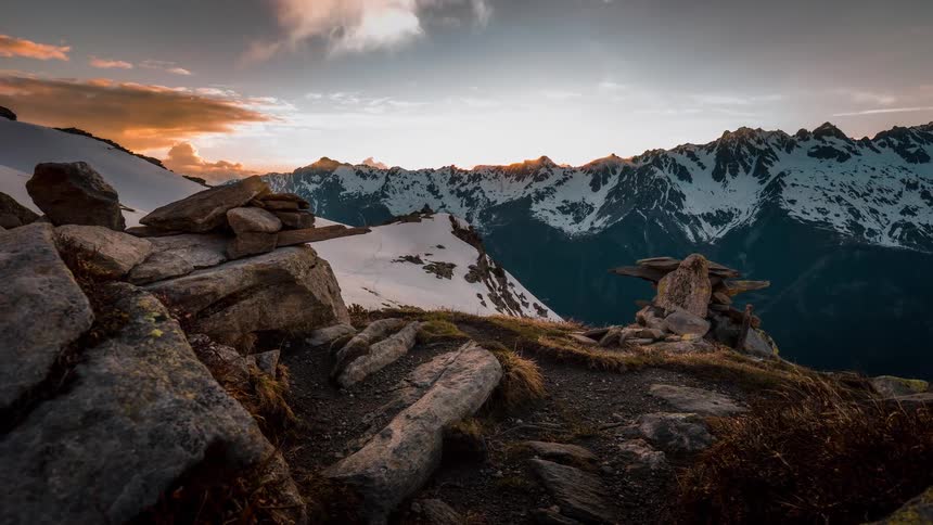 A stunning sunset timelapse from a rocky mountain peak shows golden clouds moving over a snow-covered alpine landscape