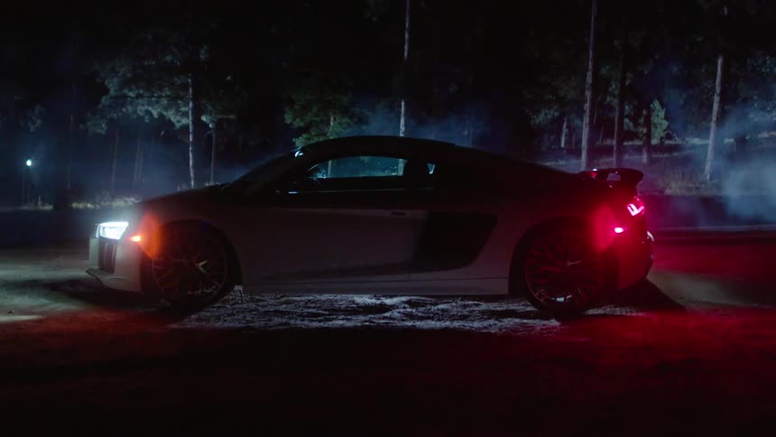 A car turns on the headlights while parked in a forest at night