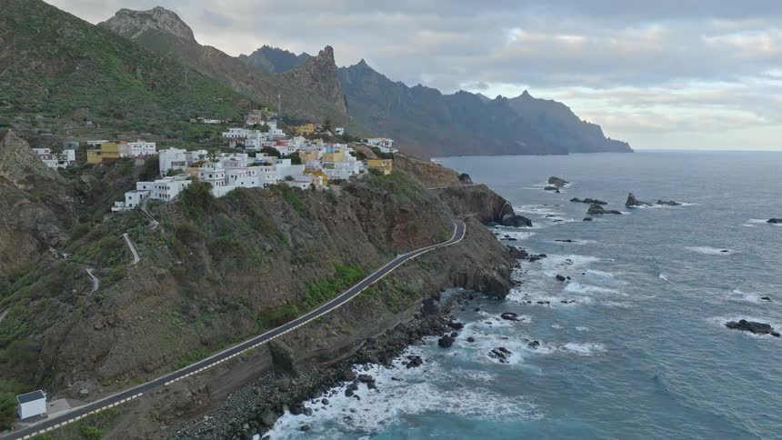 Scenic aerial flight towards a remote coastal village perched on a rugged cliff overlooking the vast ocean