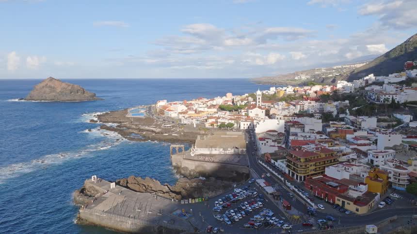 A beautiful aerial view pans across the picturesque coastal town of Garachico in Tenerife, nestled between the deep blue Atlantic and a mountainous shoreline