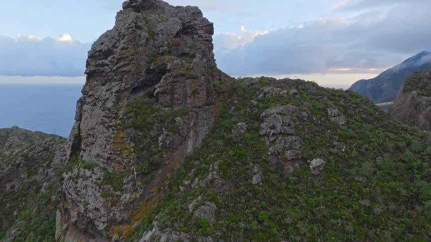 An aerial view flies past a majestic rock formation to reveal a dramatic green coastline and the vast ocean beyond