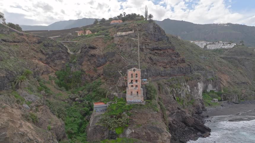 Drone footage reveals an abandoned, derelict building perched on a rugged cliffside overlooking the ocean