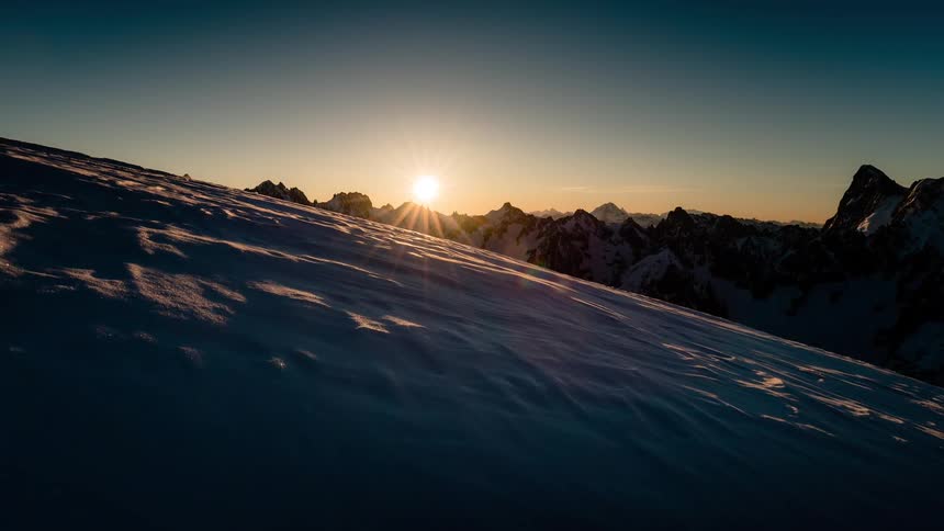 A stunning timelapse captures the sun rising over a majestic mountain range, gradually illuminating the vast, snow-covered slopes with a warm, golden light
