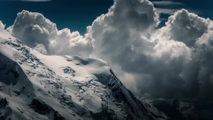 A dramatic time-lapse captures billowing clouds moving over a majestic snow-covered mountain peak