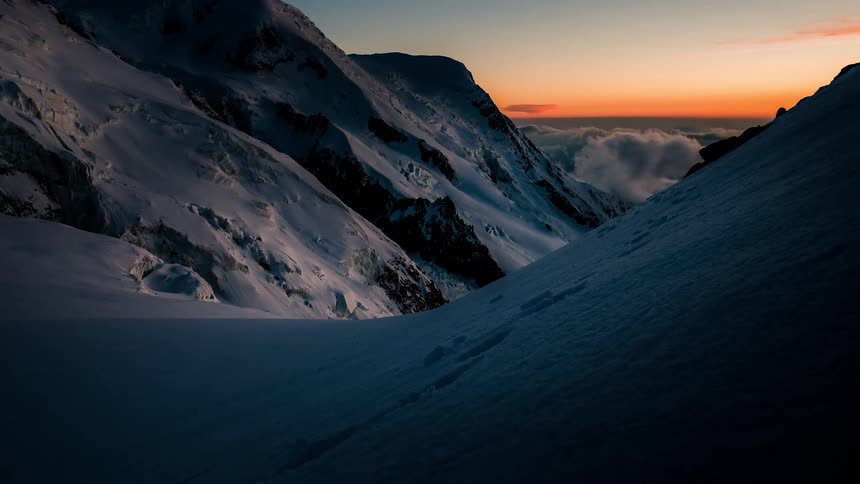 A stunning time-lapse captures the first light of dawn illuminating a majestic, snow-covered mountain valley