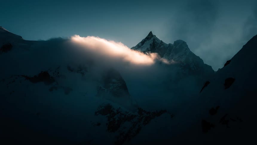 A dramatic time-lapse shows sunlit clouds moving over a majestic, snow-covered mountain peak