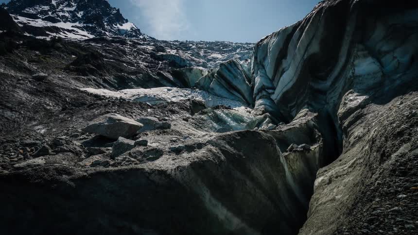 A slow, dramatic camera tilt reveals the immense and dirty face of a glacier stretching up a mountain