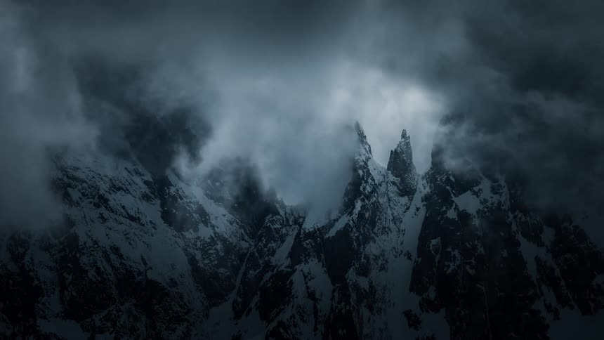 Dark, stormy clouds swirl over snow-capped mountain peaks in a dramatic time-lapse