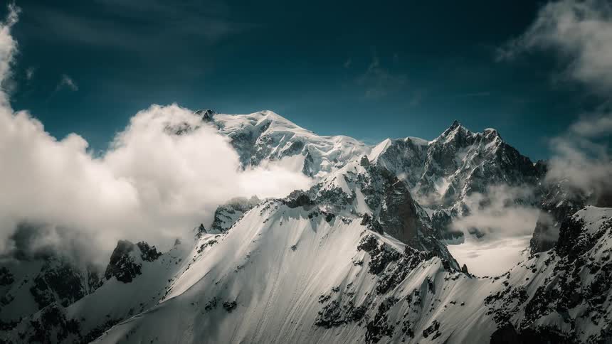 A stunning cinematic timelapse of clouds swirling around majestic, snow-covered mountain peaks under a deep blue sky