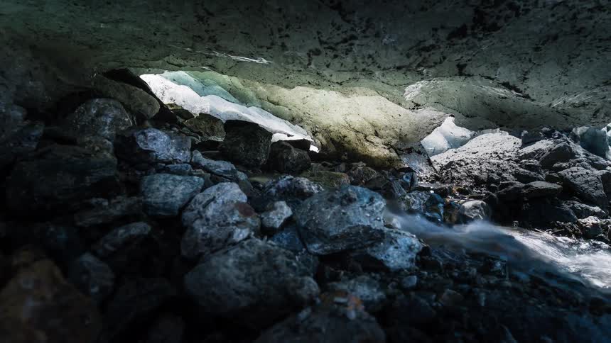 Slow reveal of a stream flowing through a rocky ice cave as the glacier melts