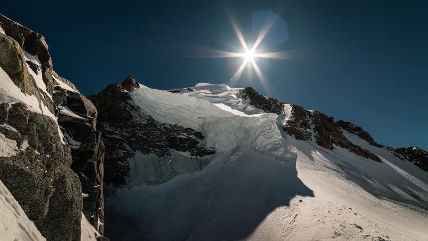 Majestic time-lapse of a sun-drenched glacier high in the snowy mountains as the sun moves across a clear blue sky