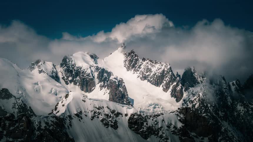 A dramatic time-lapse of clouds flowing over majestic snow-covered mountain peaks under a deep blue sky