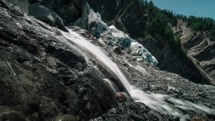 A powerful timelapse shows a glacial meltwater stream cascading down a rugged, rocky mountainside in the Alps