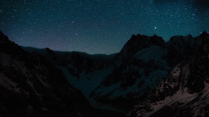 A majestic timelapse captures the Milky Way and a sea of stars moving across the night sky as clouds part over a snow-covered mountain range