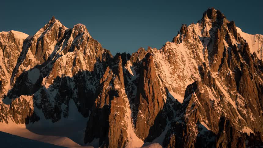 A stunning cinemagraph captures the majestic snow-capped peaks of a mountain range glowing with warm alpenglow during sunrise
