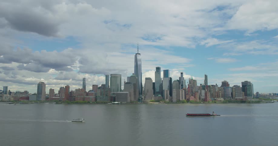 Boats travel along the river with the iconic Lower Manhattan skyline and One World Trade Center in the background on a partly cloudy day