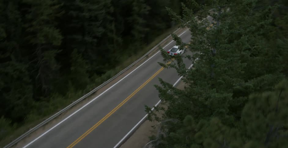 A white car drives up a mountain road and takes up both lanes