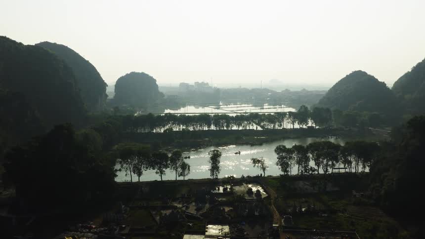 A picturesque aerial shot captures a hazy river valley with boats and a distant town nestled between silhouetted mountains