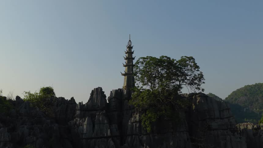 A majestic stone pagoda stands atop a rugged mountain cliff under a clear morning sky