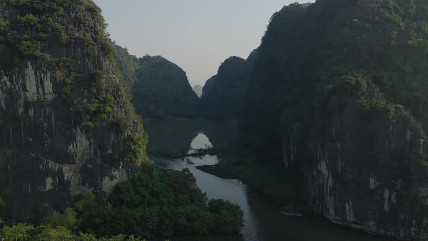 Slowly pushing in aerial shot over a tranquil river valley surrounded by majestic green limestone mountains in Vietnam